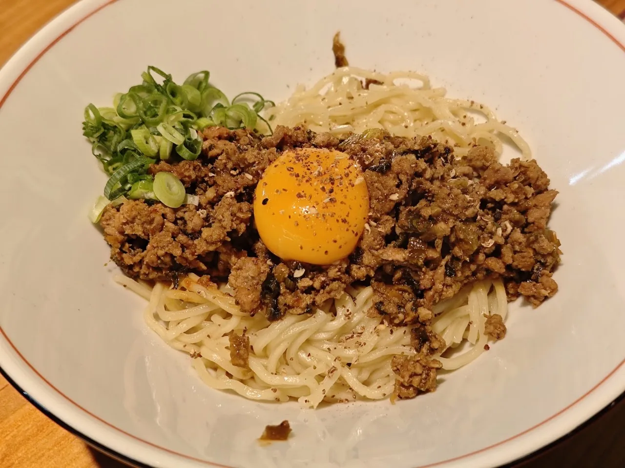 Bowl of noodles topped with minced meat and a raw egg yolk