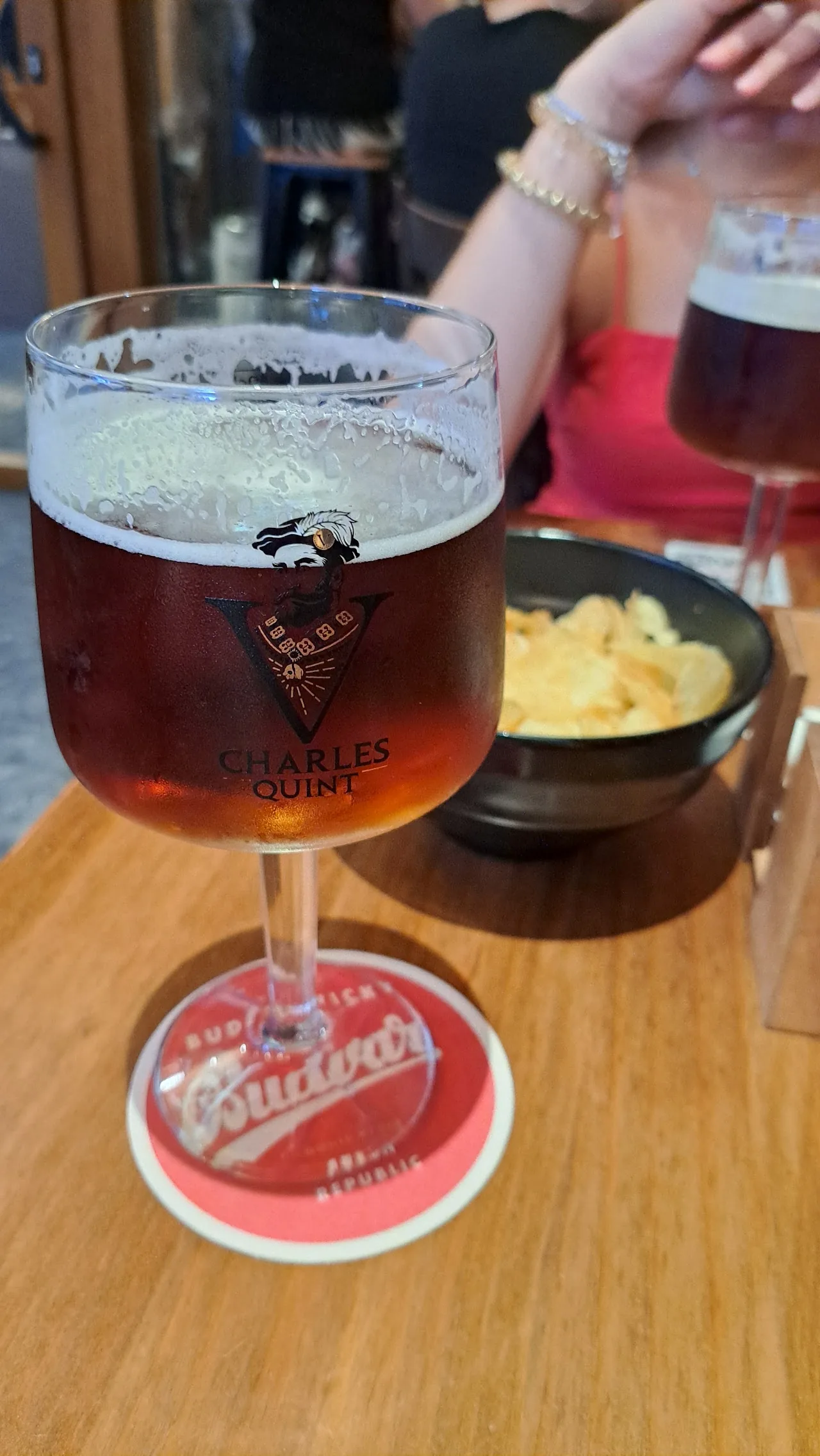 A glass of amber beer on a coaster next to a small bowl of snacks