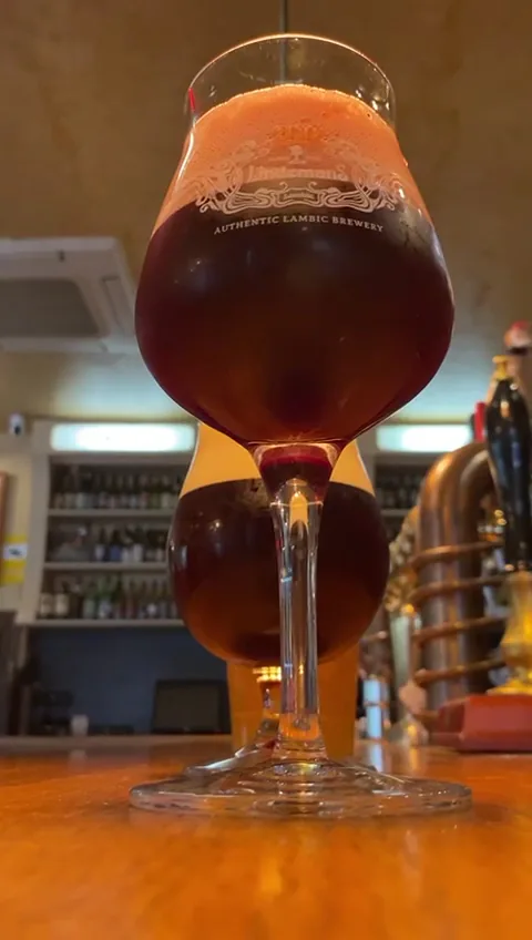 Two glasses of dark amber beer with foam on top on a wooden bar