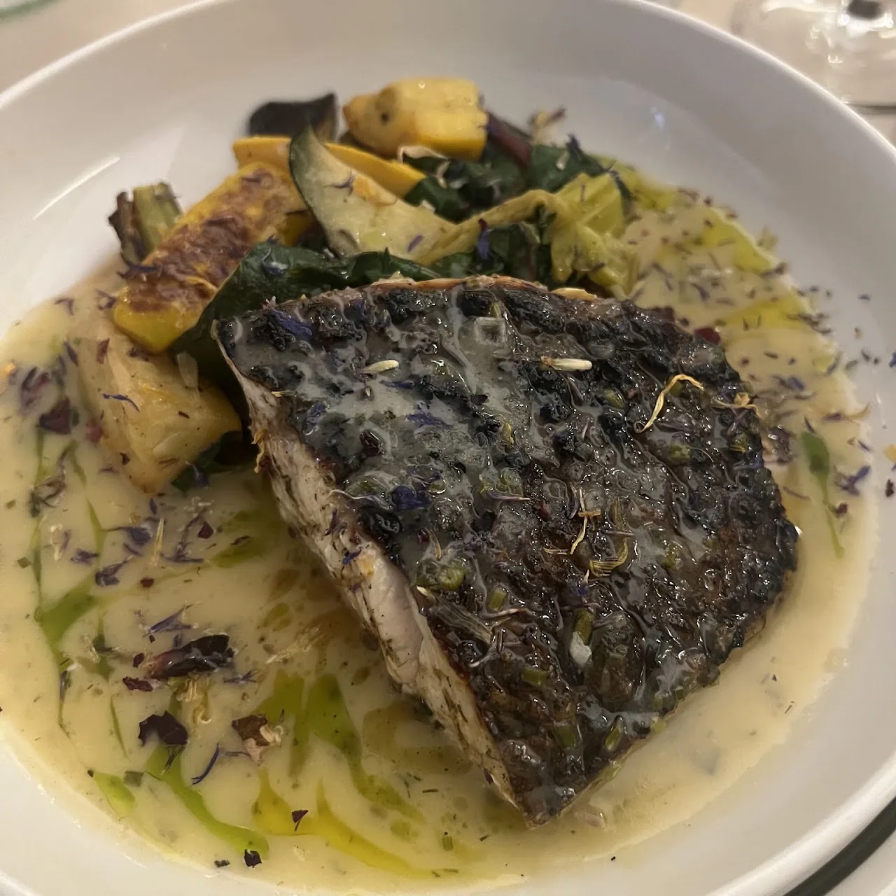 Grilled fish fillet plated with sautéed vegetables