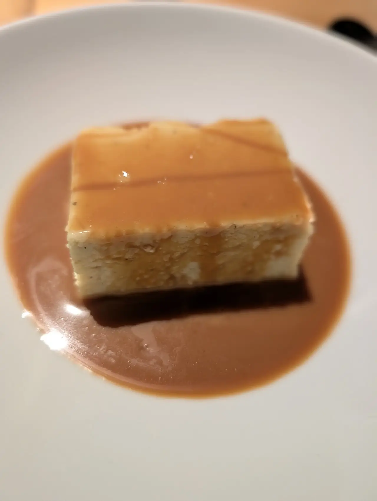 A caramel-glazed dessert cake in a pool of caramel sauce on a white plate