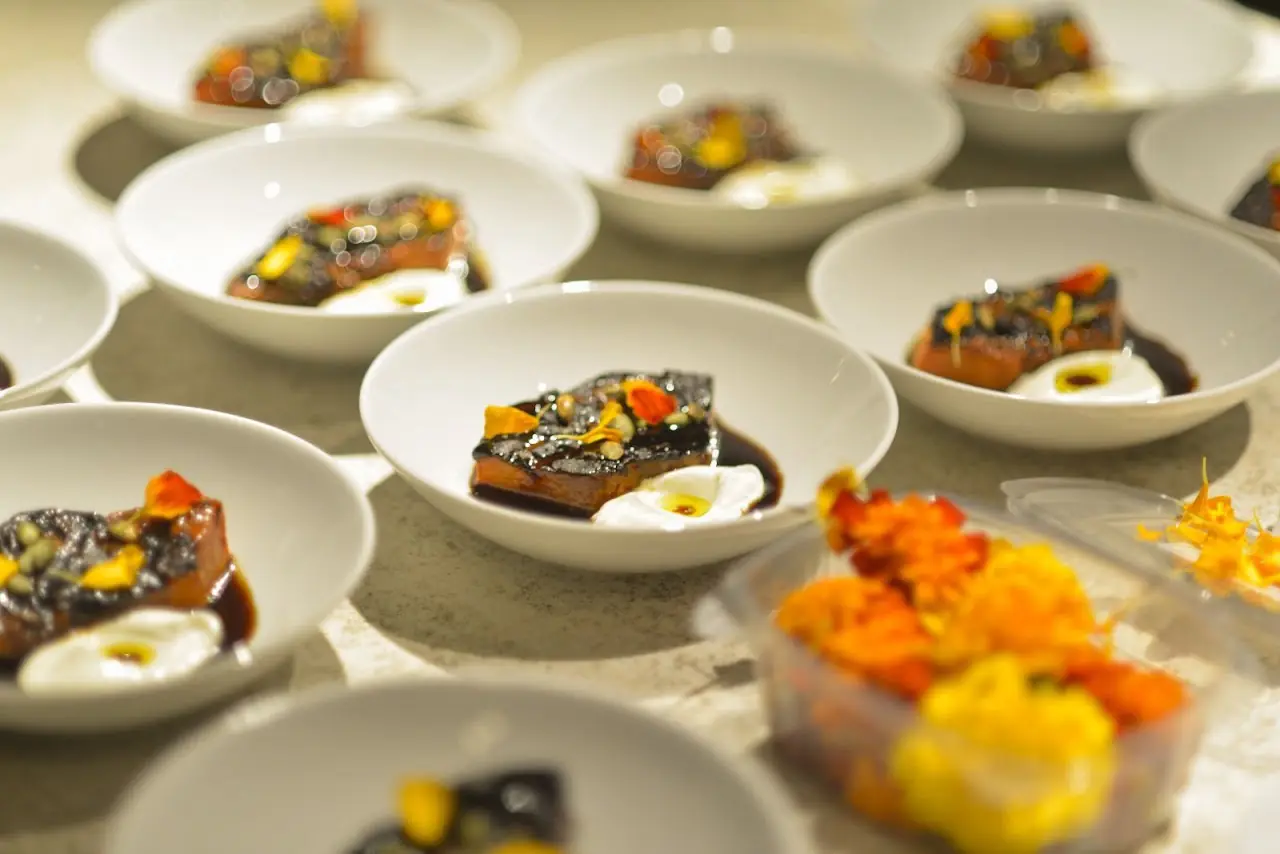 Several small white bowls of a plated dish with dark sauce and colourful garnish