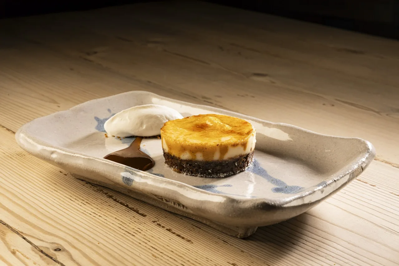 A pale oblong dish holding a small round baked dish and a smear of dark sauce