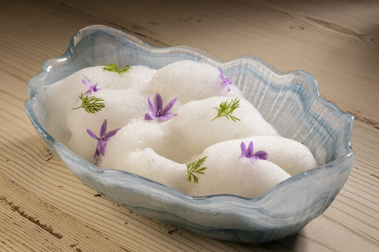 A blue-rimmed glass bowl holding white foam scattered with small purple flowers