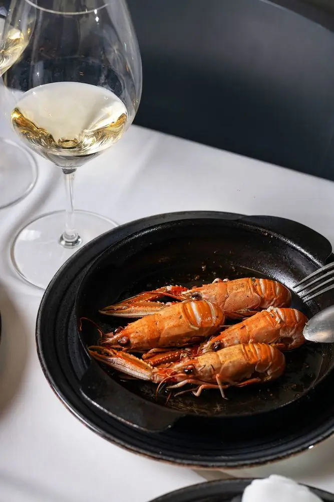 Grilled langoustines served in a dark cazuela dish beside a glass of white wine at O'Peregrino - Gastromar