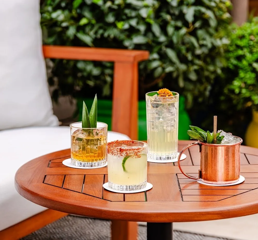 Three cocktails and a copper mug on a round wooden table on a terrace