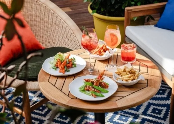 Two plates of food and two cocktails on a round wooden table on a terrace