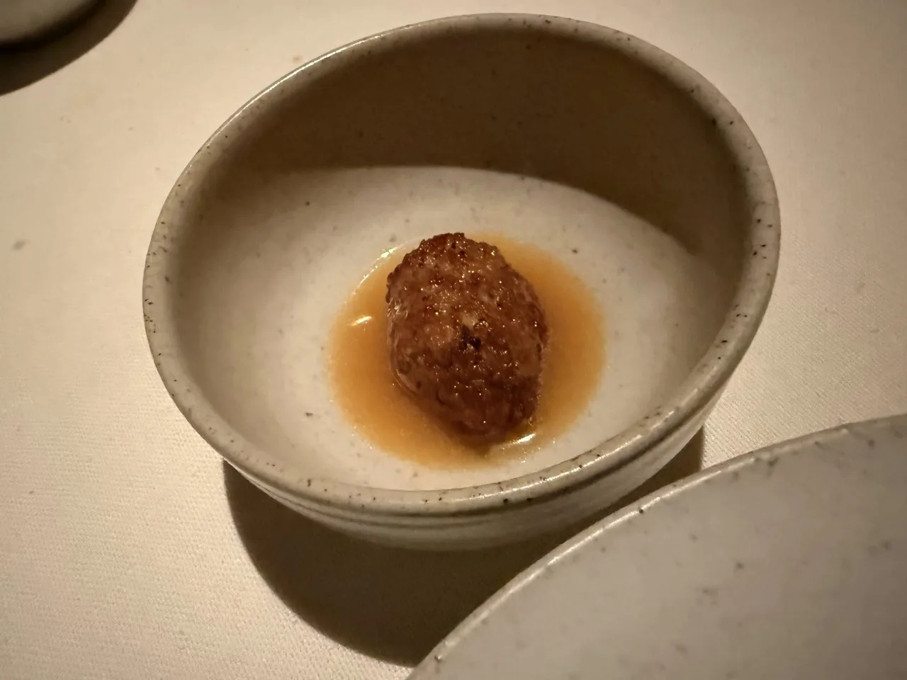 A stone-coloured bowl holding a small browned round of food in a light broth