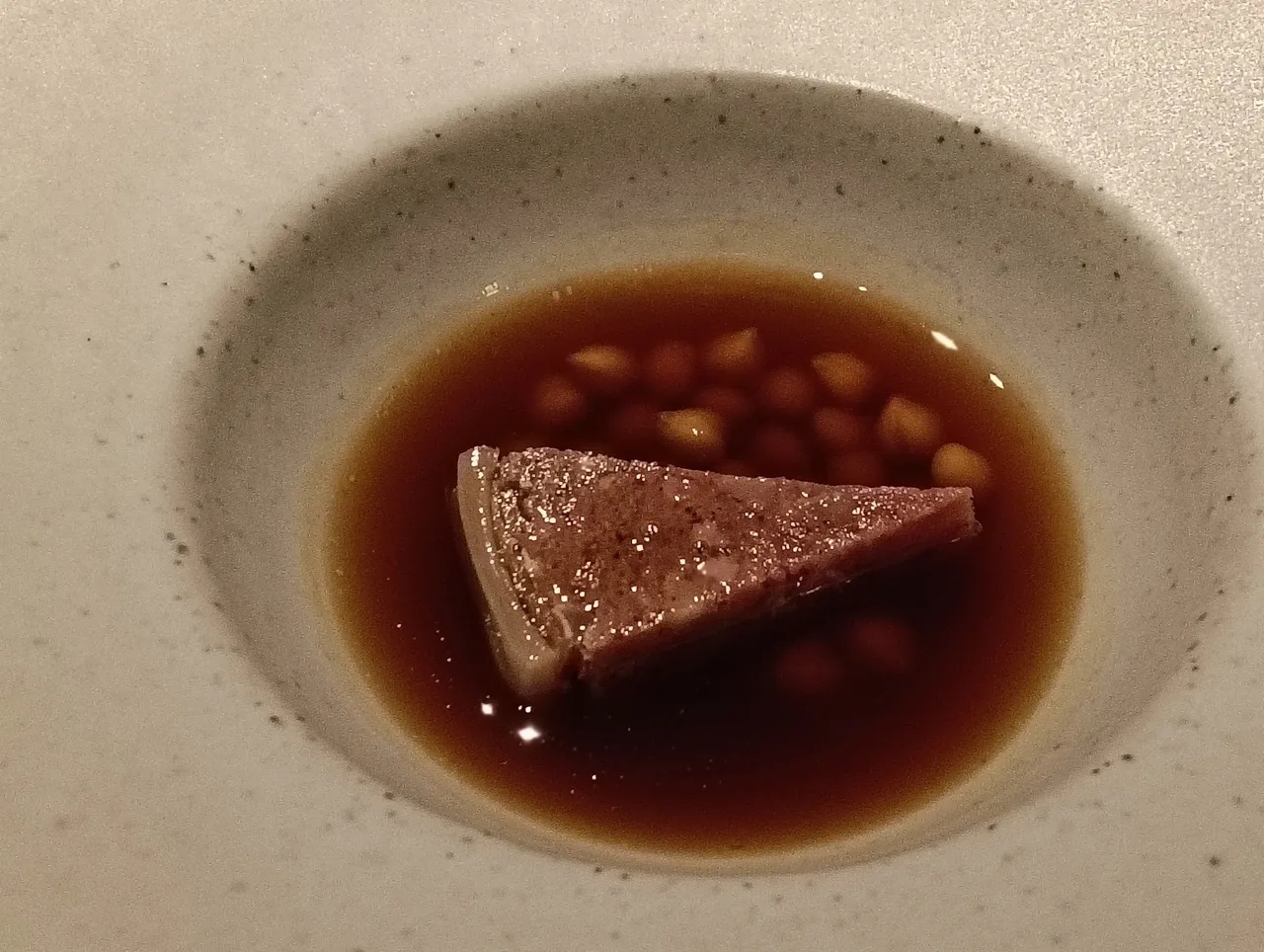 A cream bowl with a triangular piece of dark meat in a brown broth with beans