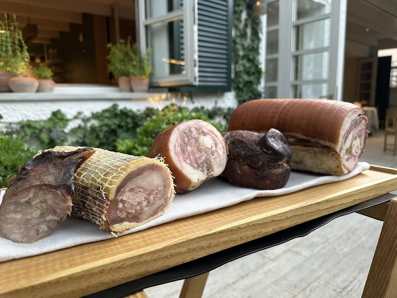 A wooden board with several rolled and tied cured meats