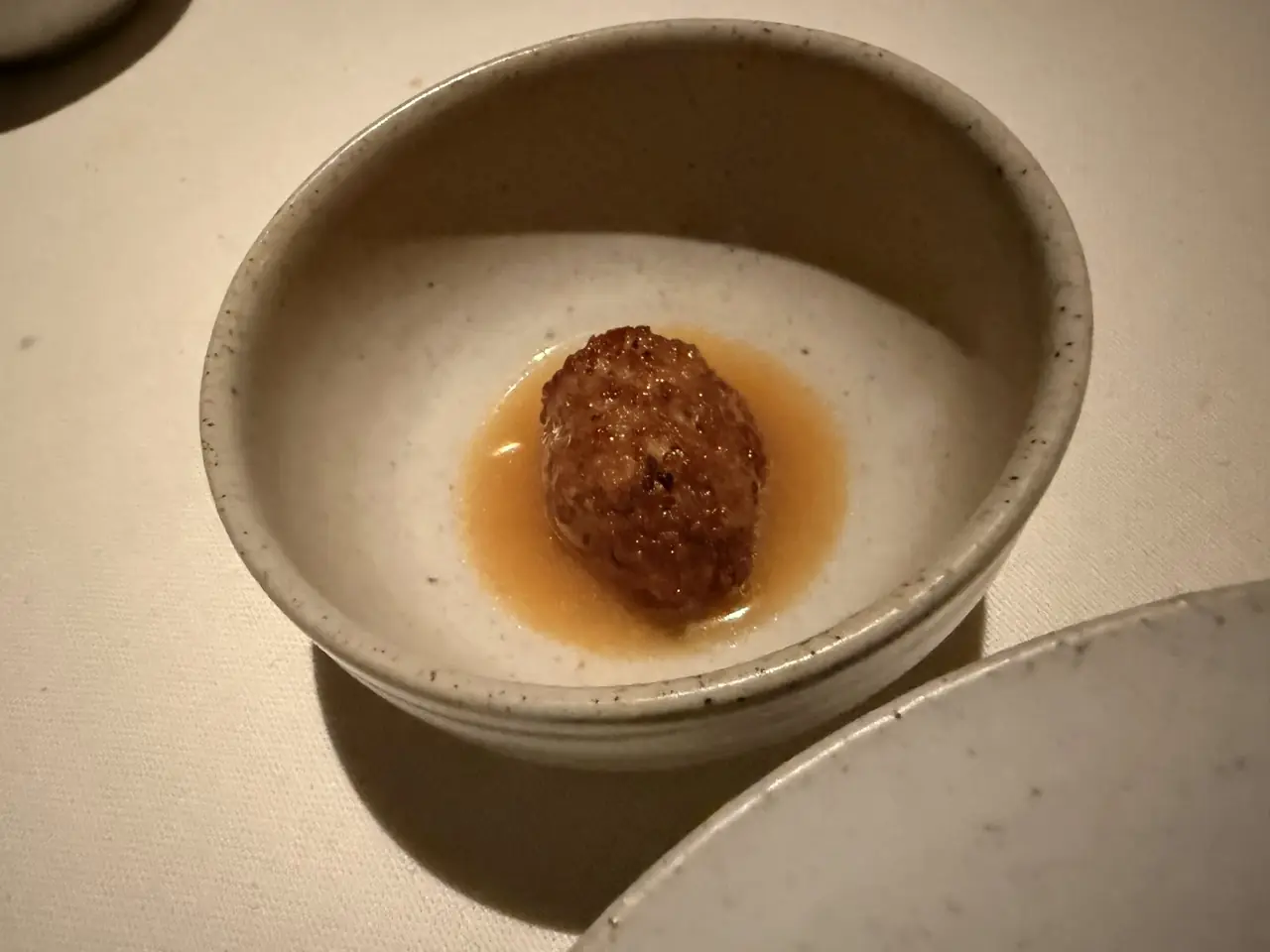 Single meatball-like croquette in savory broth in small ceramic bowl