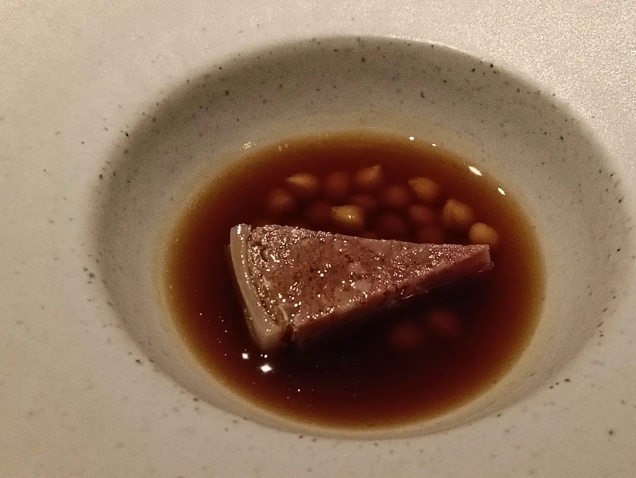 Triangular slice of terrine in broth with legumes in small ceramic bowl