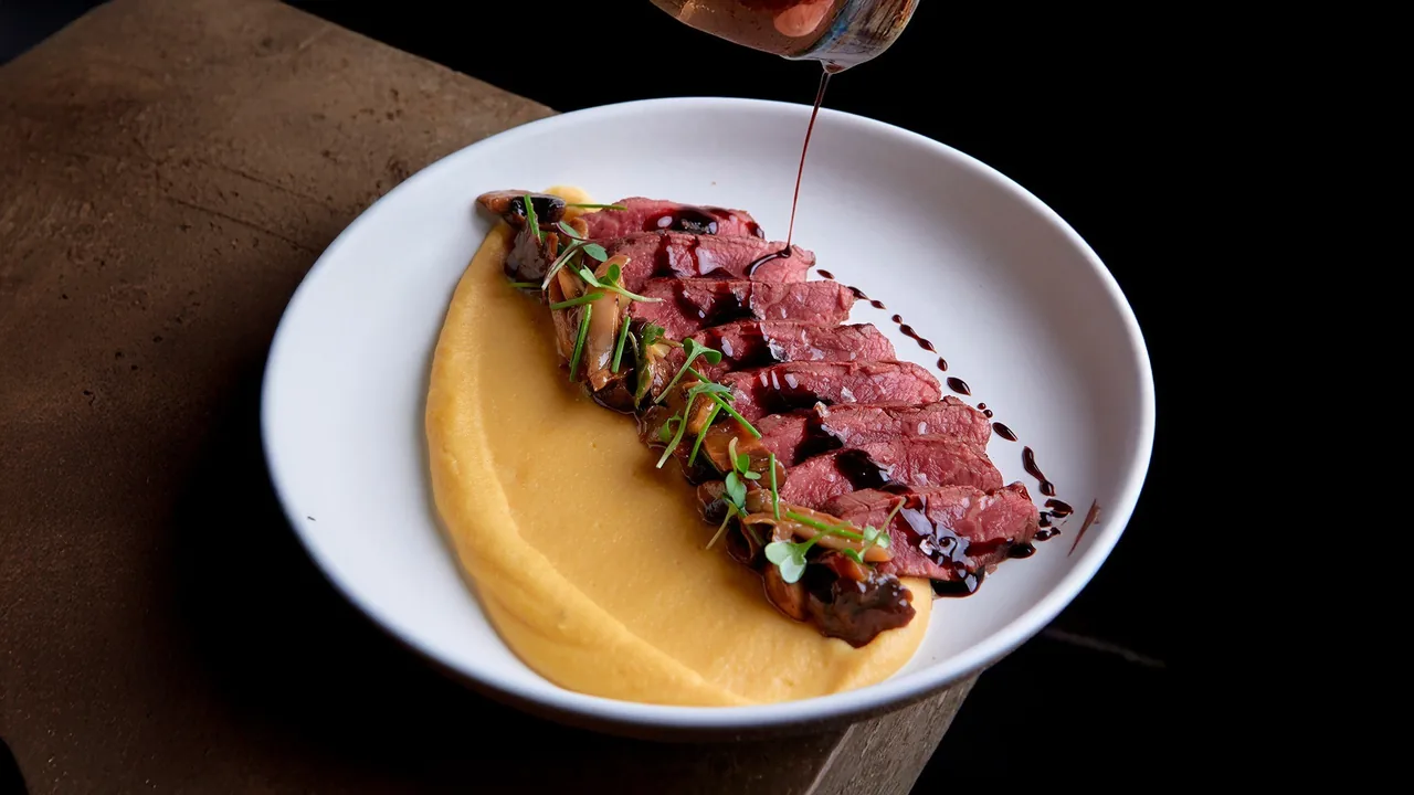 Sliced seared beef over a yellow purée on a white plate against a dark background