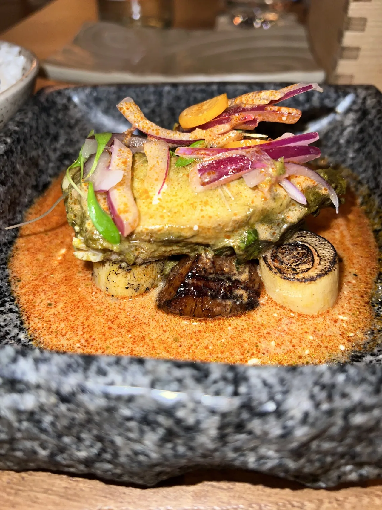 Plated dish with pickled vegetables and herbs over a rice base, served on a stone platter