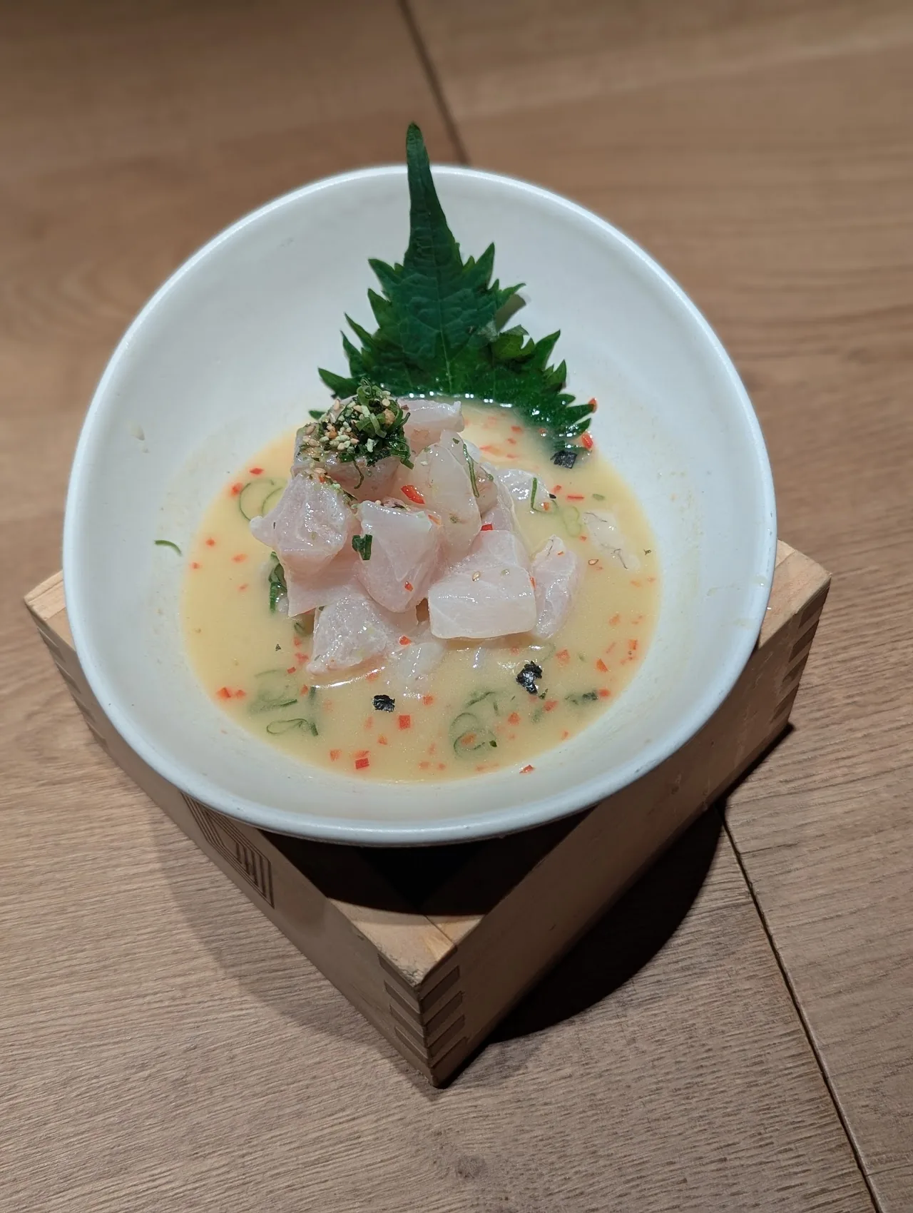 White bowl with sliced fish in a creamy broth, garnished with a shiso leaf