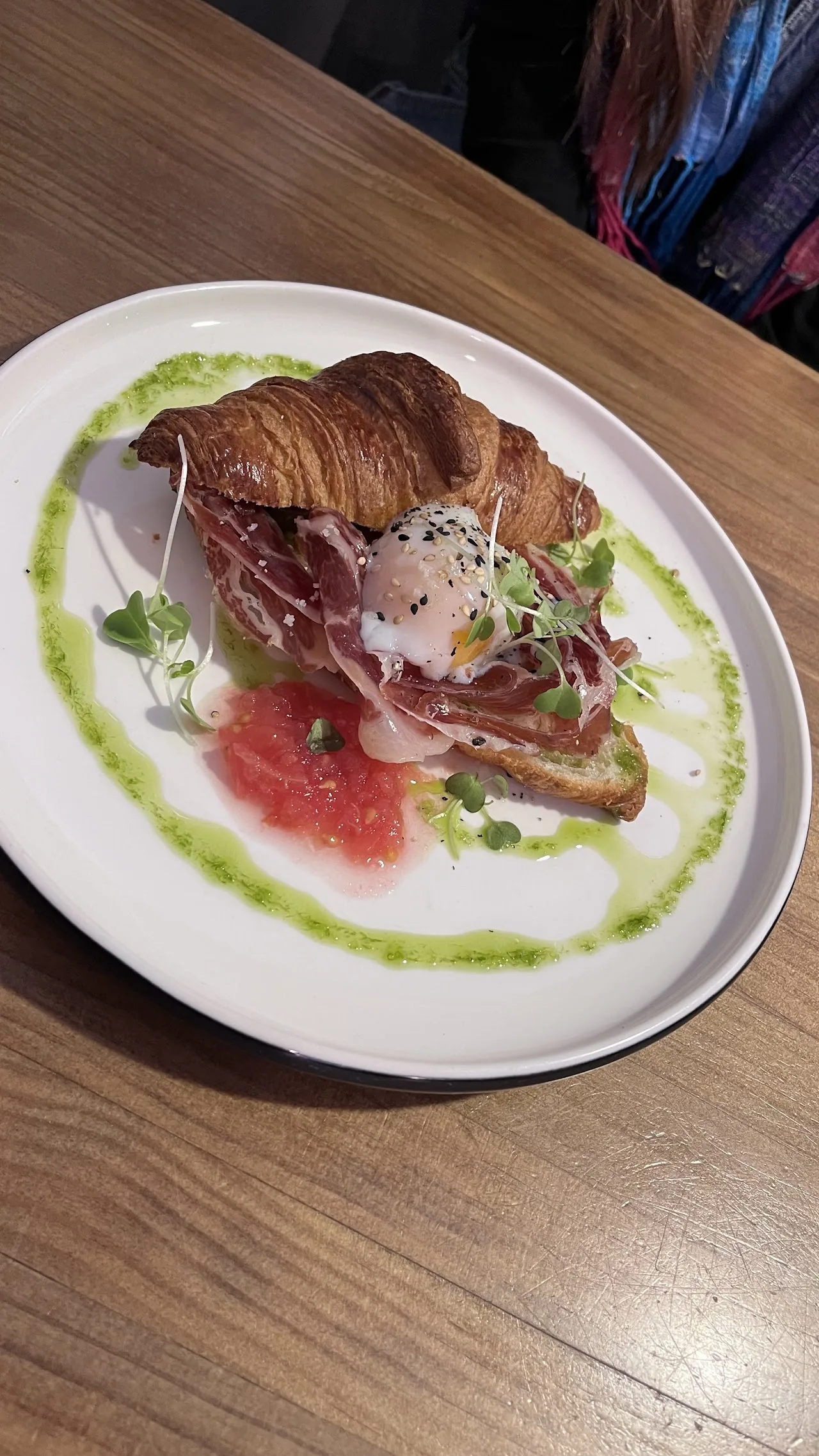 A croissant sandwich with prosciutto and greens, plated with dressing