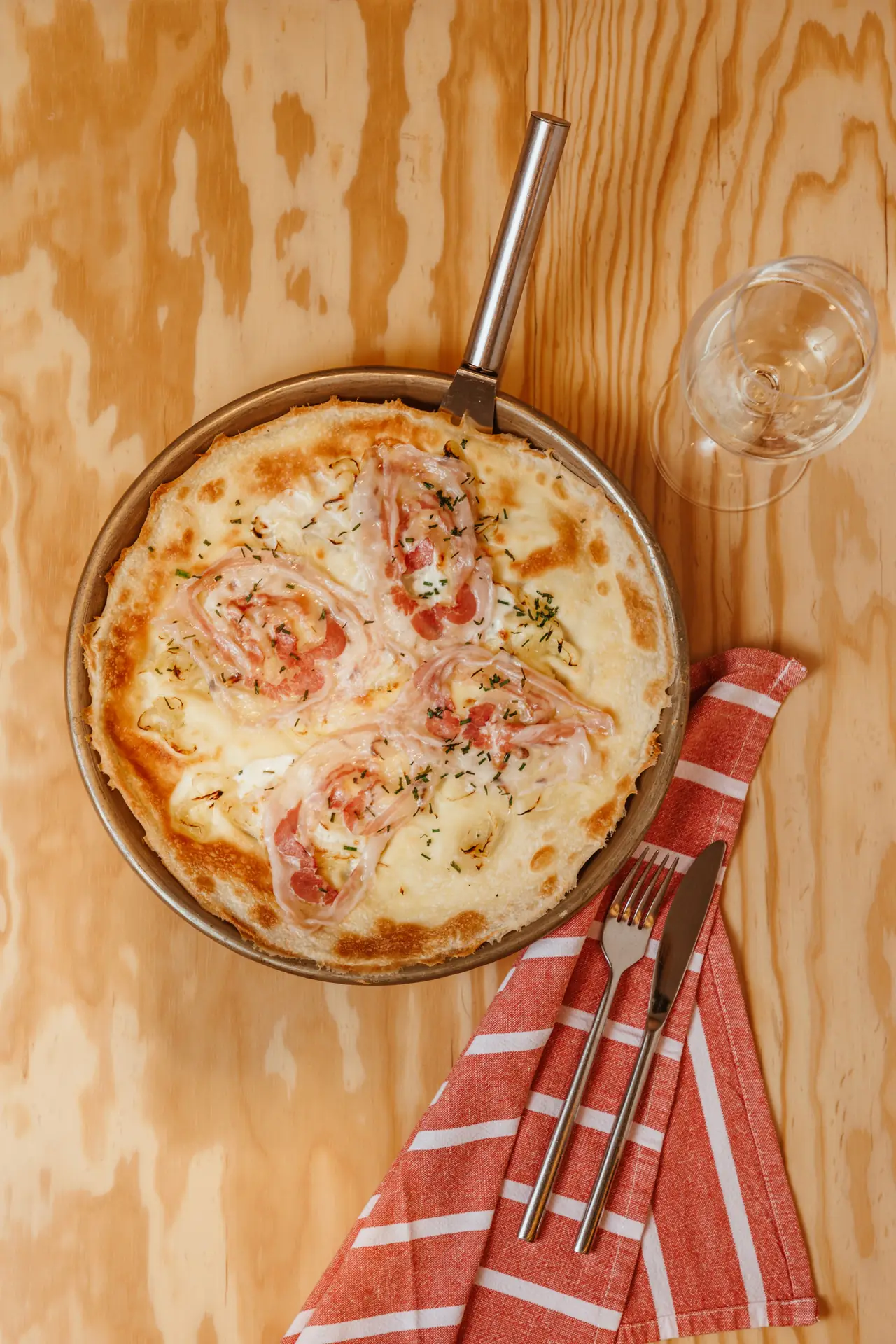 Baked focaccia-style dish topped with rolled prosciutto, melted cheese, and chives in a metal pan, served with a glass of white wine, at Ostaia