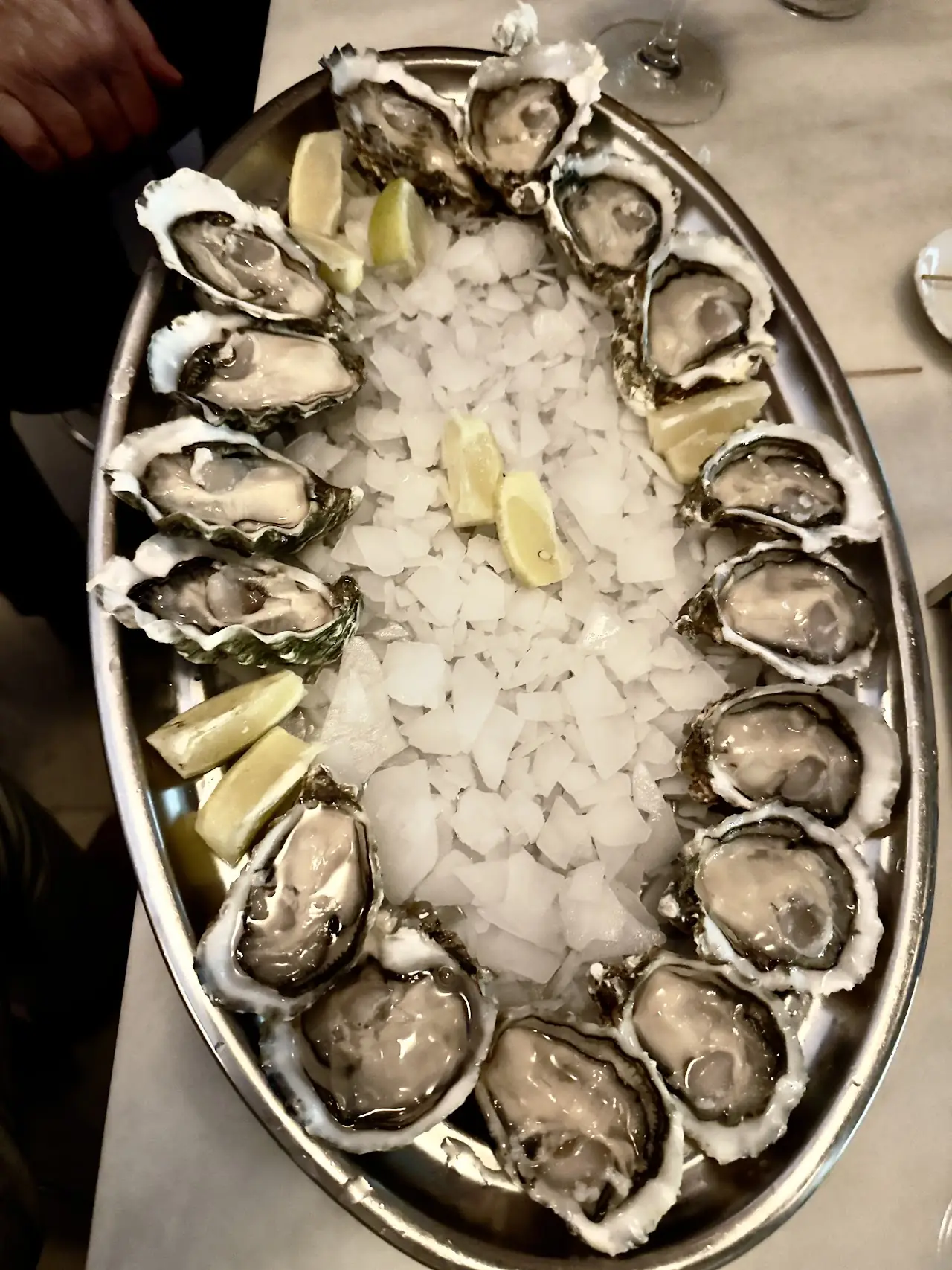 An oval platter of oysters on a bed of ice with lemon wedges