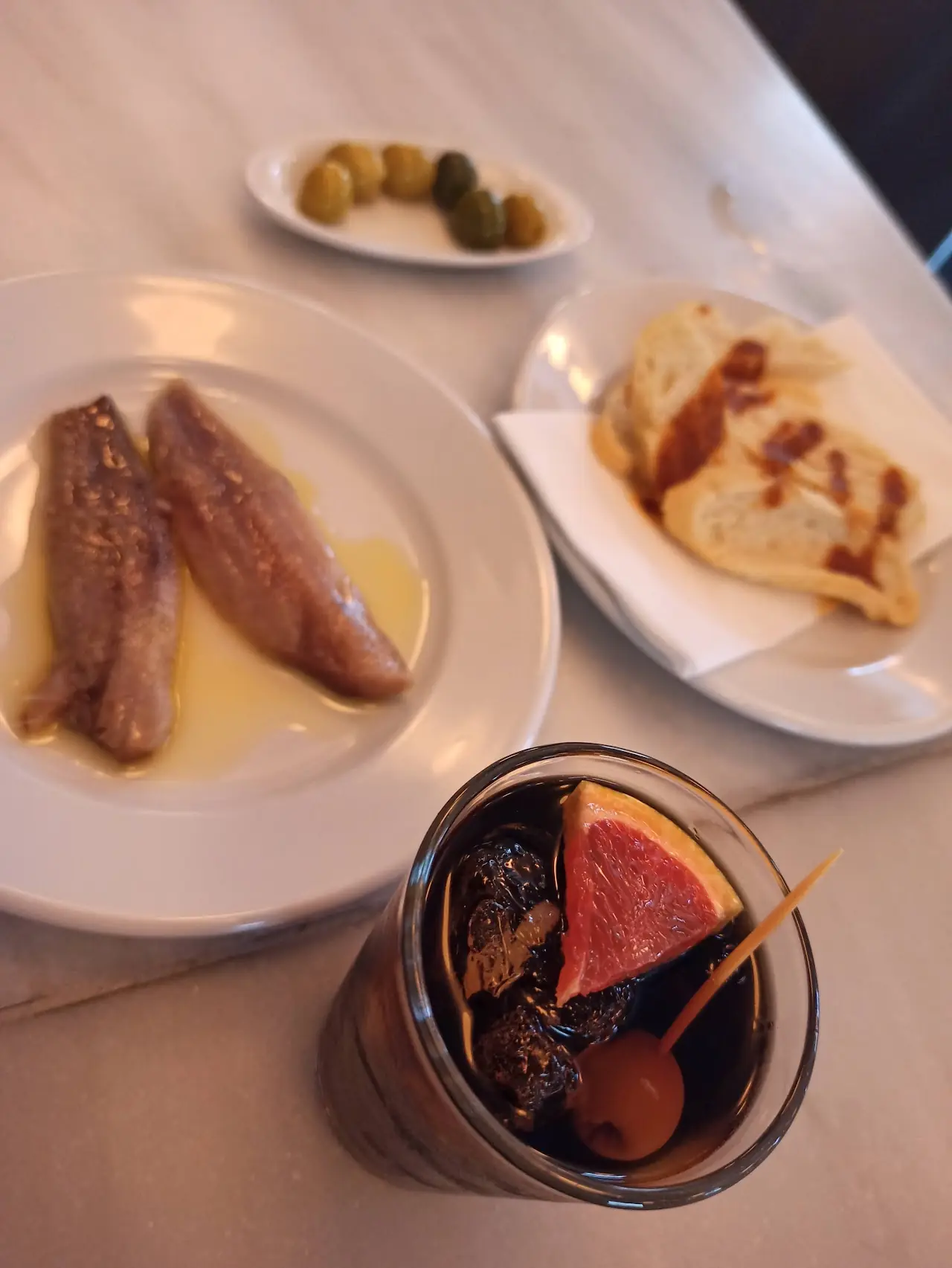 Small plates of grilled fish and a filled pastry with olives and a red drink
