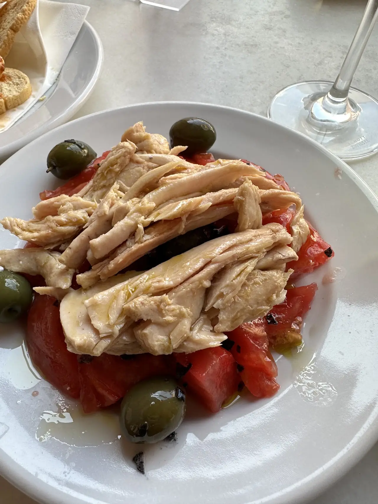 A white plate of shredded fish with tomato and green olives