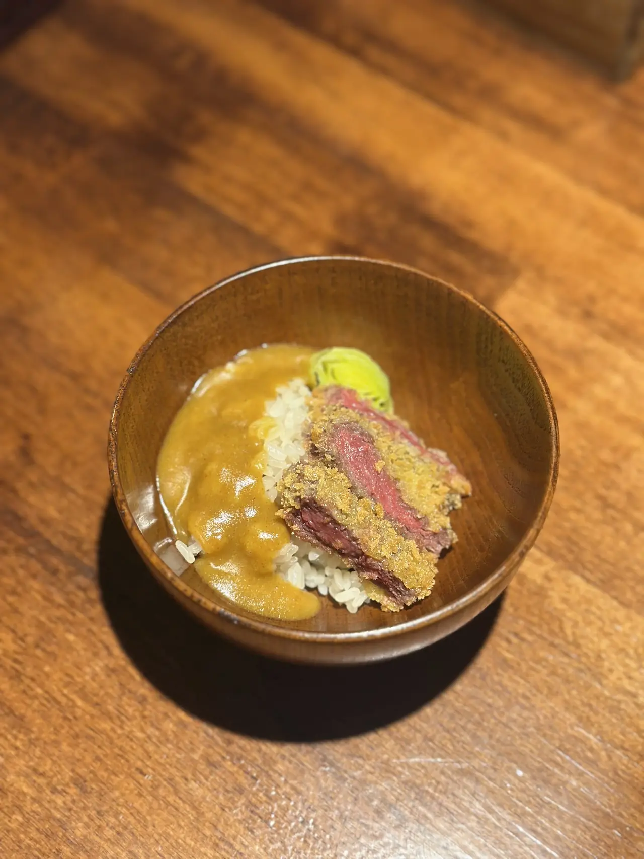 Breaded fried beef cutlet with curry sauce over rice in a wooden bowl