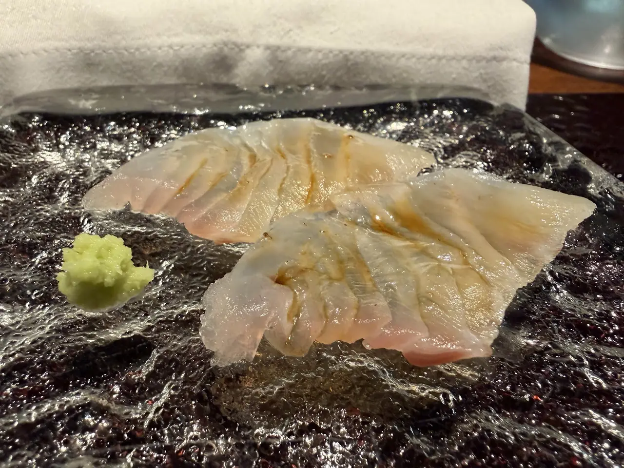 Thin sashimi slices with soy glaze fanned out on ice, served with a dab of wasabi