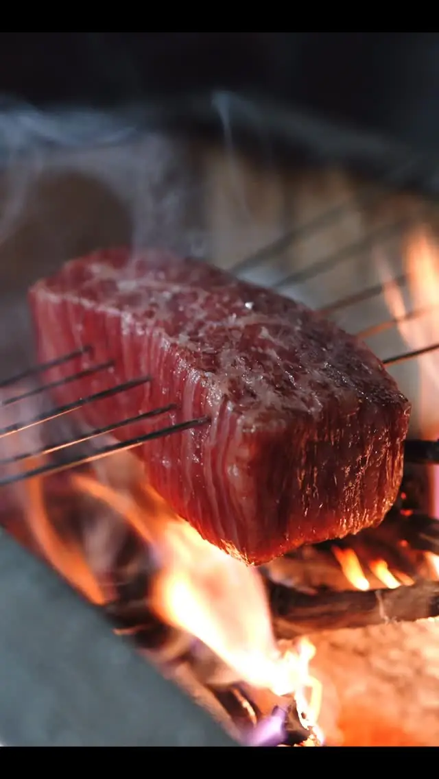 Close-up of a thick cut of meat searing on skewers over an open charcoal flame