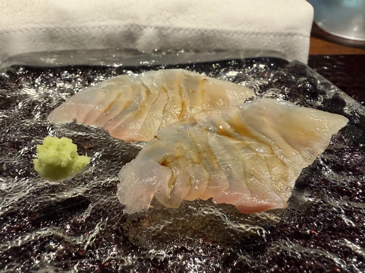 Slices of raw white fish on dark seaweed with a dab of wasabi