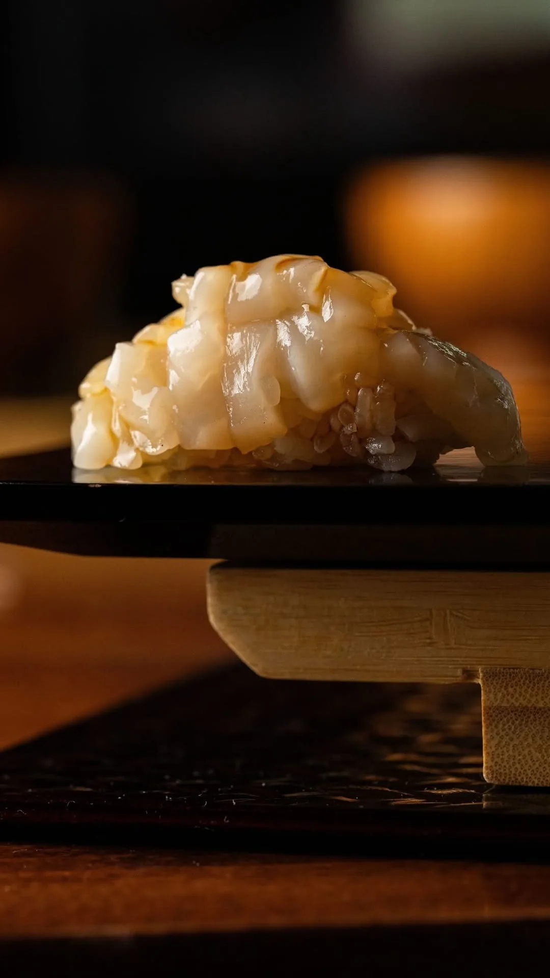 A nigiri topped with pieces of pale shellfish on a black tray
