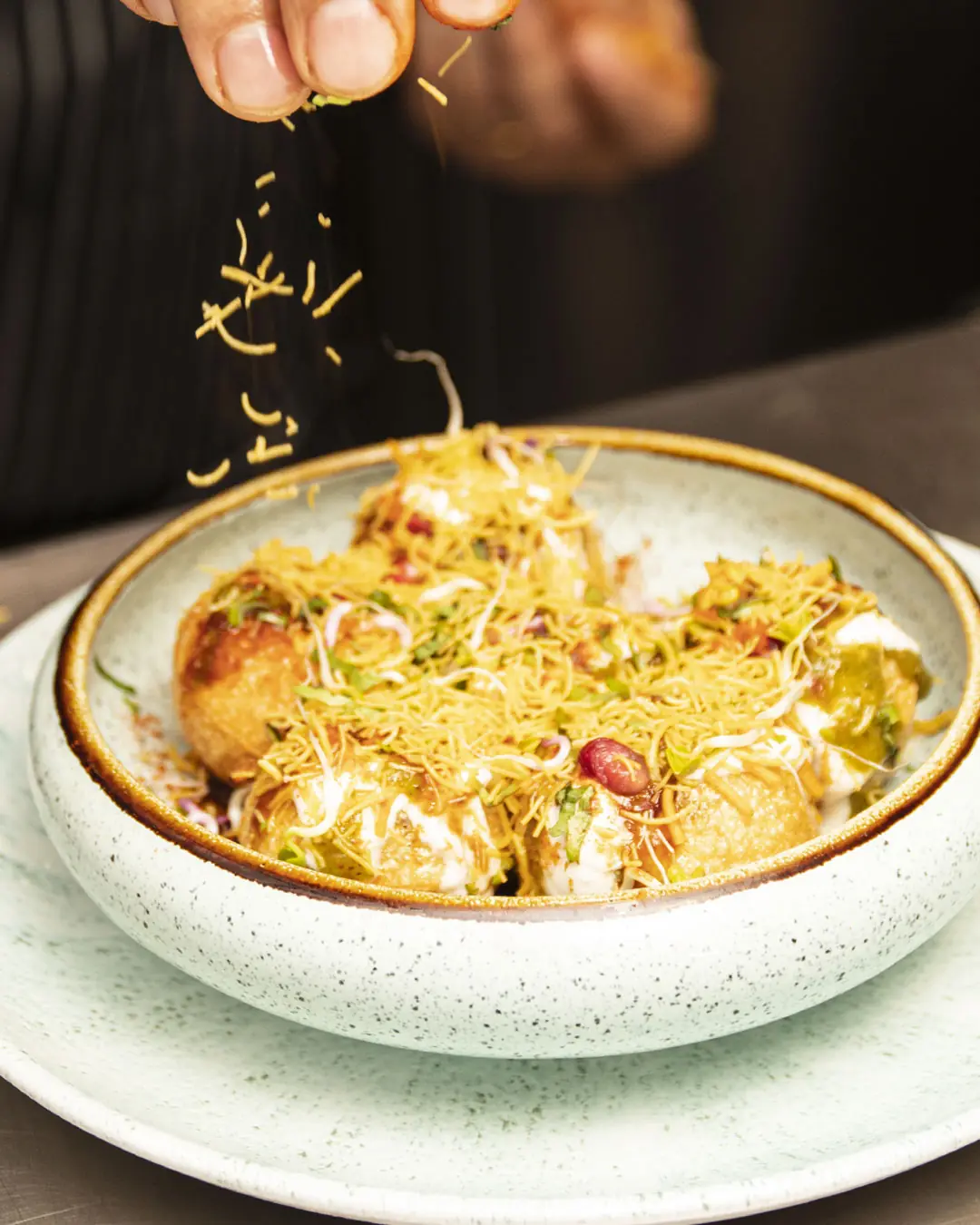 A bowl of dahi puri chaat, crisp puri shells filled with potato and topped with yogurt, tamarind chutney, sev, pomegranate seeds, and fresh herbs, at Out of India