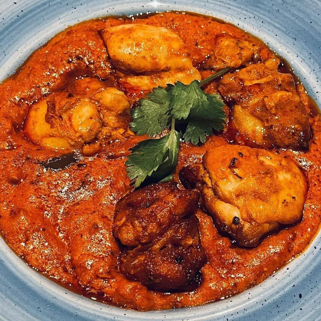 A close-up bowl of chicken tikka masala in a red-orange curry sauce, garnished with fresh coriander, at Out of India