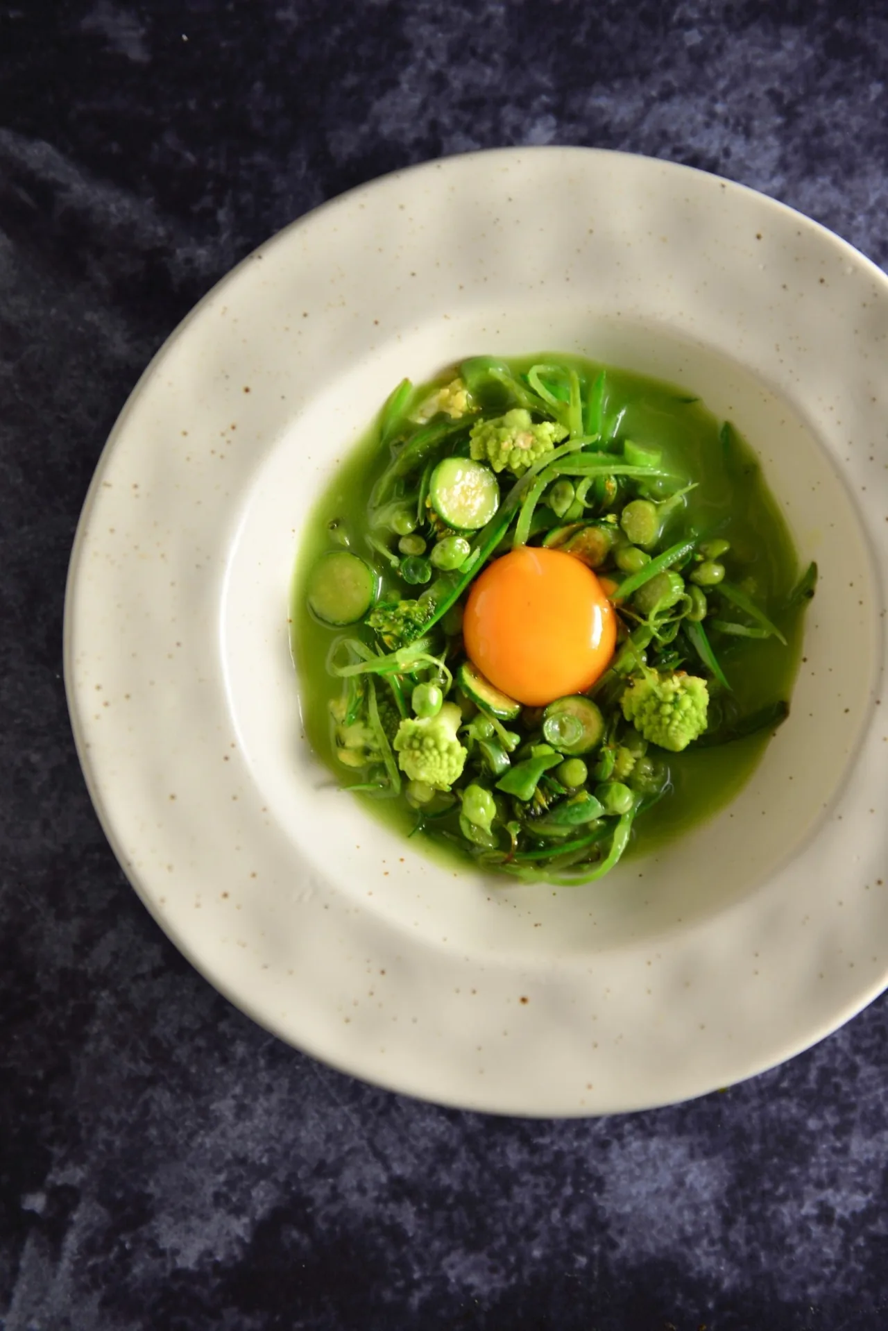 A green dish topped with an egg yolk in a shallow bowl on a dark surface