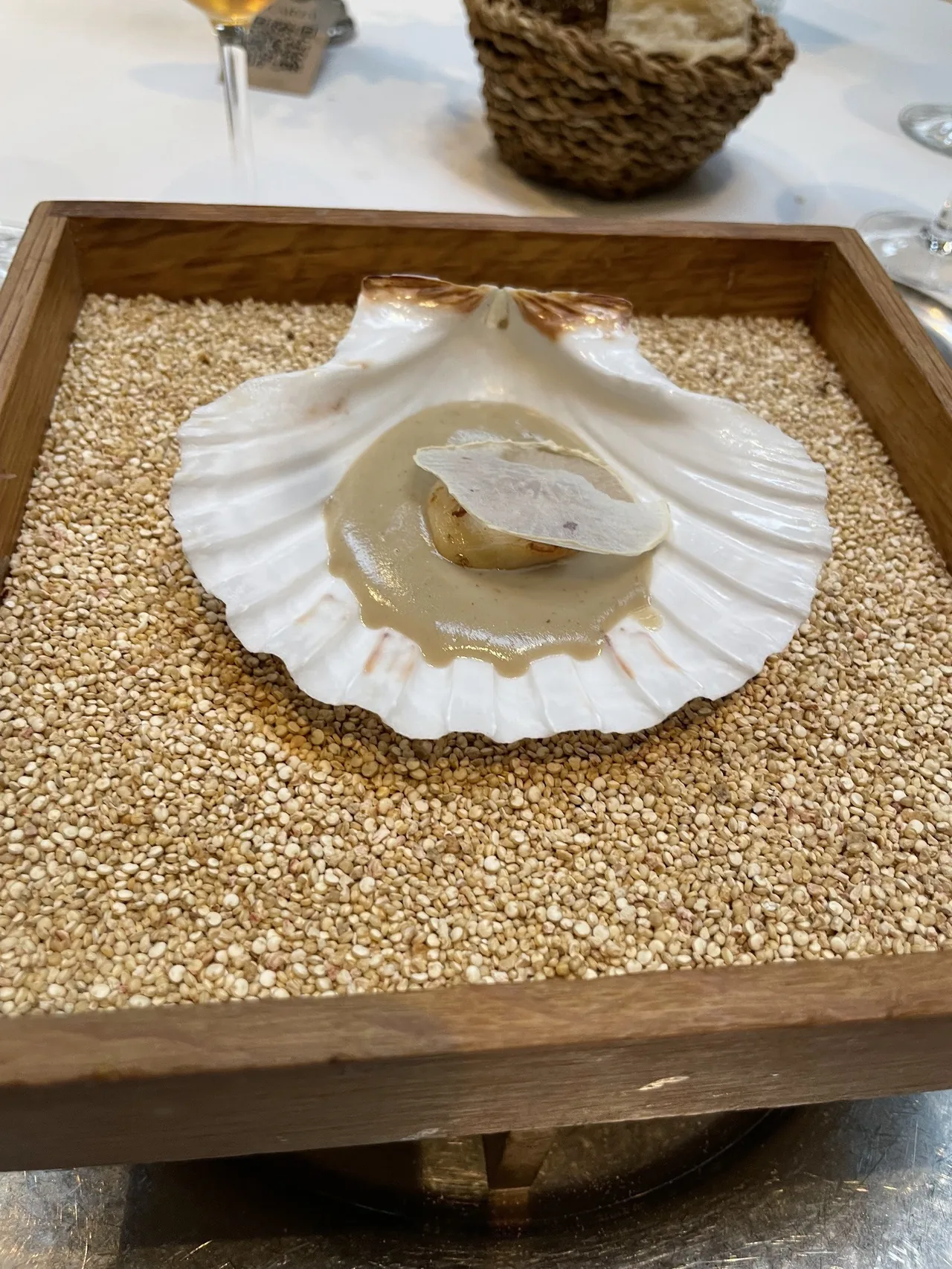 A scallop shell resting on grains in a square wooden tray