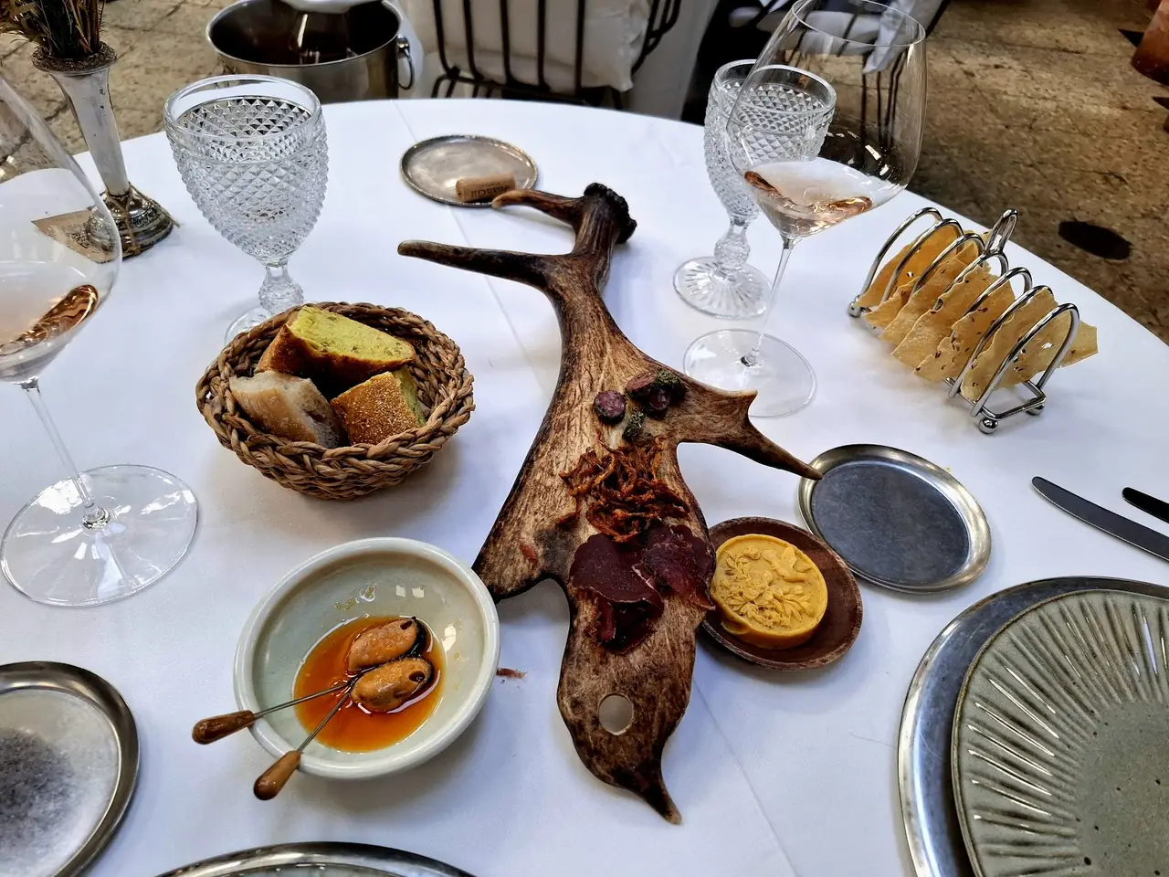 Antler-shaped board with cured meats, pate, pickled mussels, bread basket and wine glasses on table