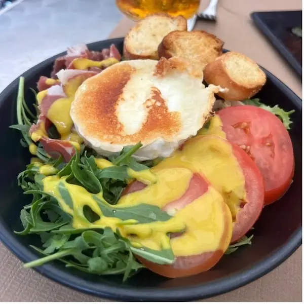 Salad of arugula, sliced tomato, and cured ham topped with a grilled round of goat cheese and mustard vinaigrette, served with toasted baguette slices, at Oviso.