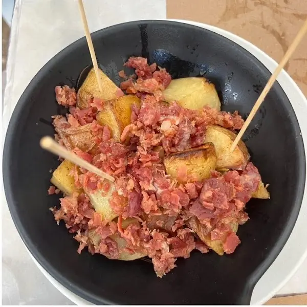 Bowl of fried potato cubes topped with chopped cured Iberian ham, skewered with wooden picks, at Oviso.