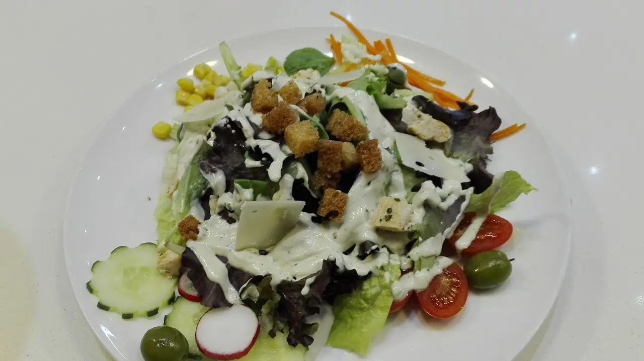 Green salad with chickpeas, cherry tomatoes, cucumber and a dollop of dressing on a white plate, at Ovo.