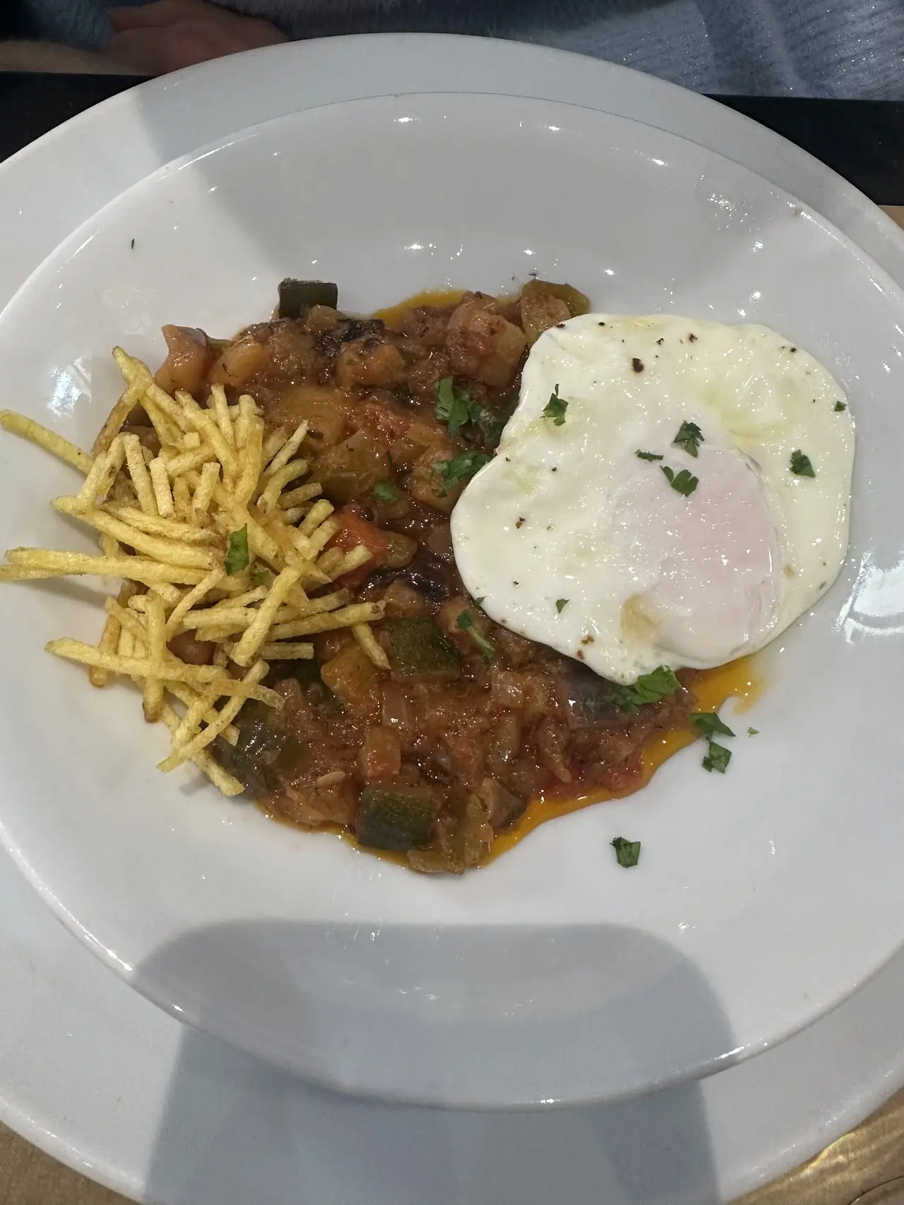 Stew served with shoestring potatoes and a fried egg on a white plate, at Ovo.