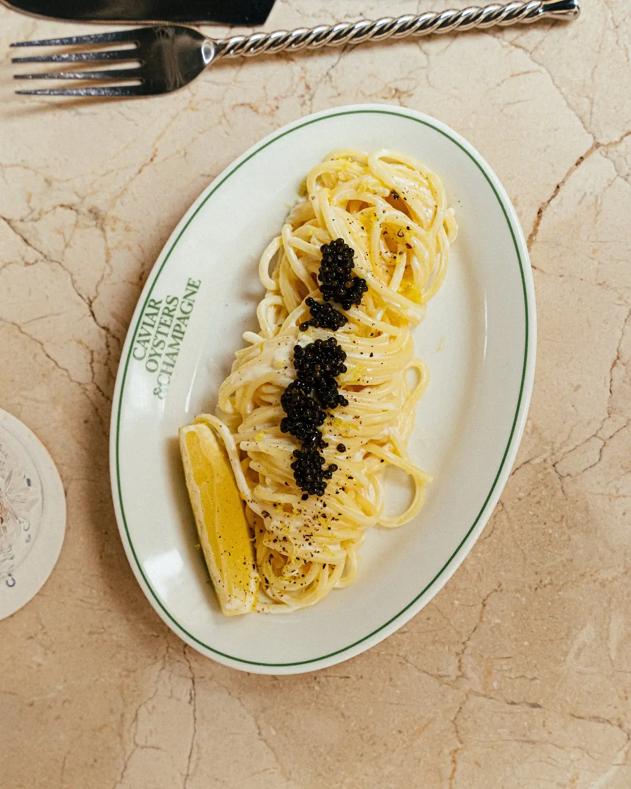 Spaghetti tossed in a creamy butter sauce with a line of black caviar and a charred lemon wedge, on an oval plate, at Oysters Menorca
