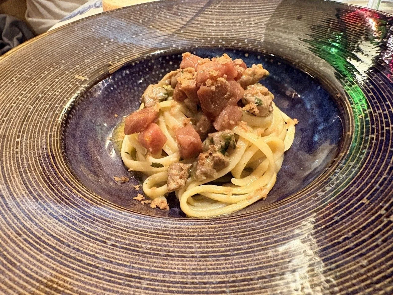 A dark plate of long pasta with pieces of meat and a light sauce