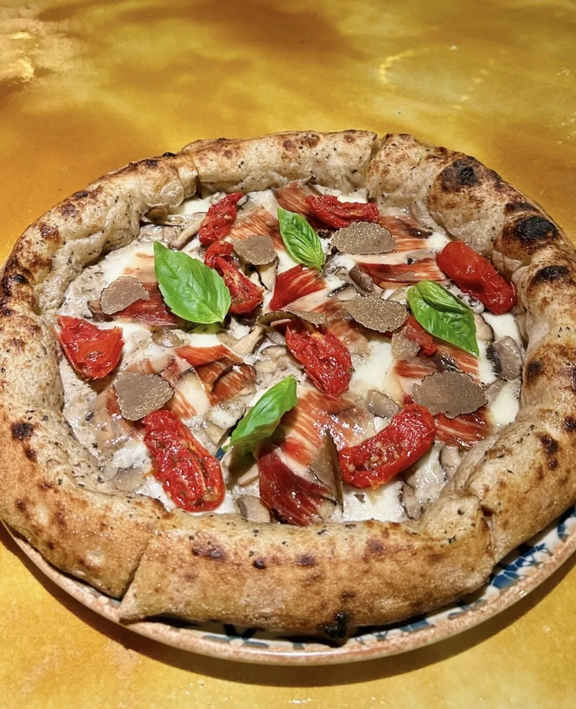A baked pizza with tomato slices, basil leaves and shavings on top