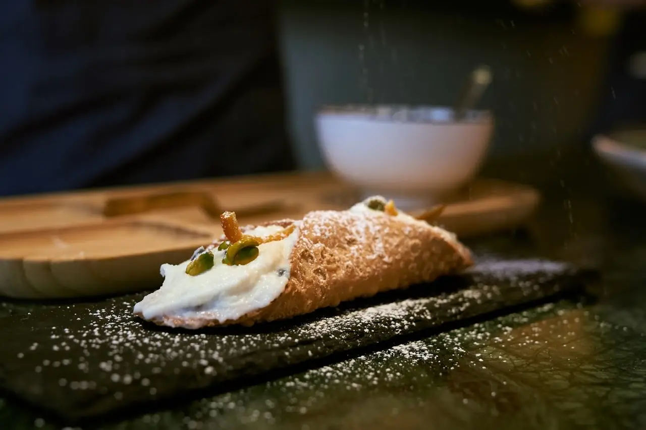 A cannoli filled with cream, dusted with powdered sugar, on a wooden board