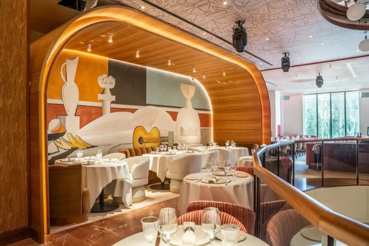 Elegant restaurant dining room with a large modernist mural of a guitar and vases, white-linen tables, curved wood archway and dramatic lighting