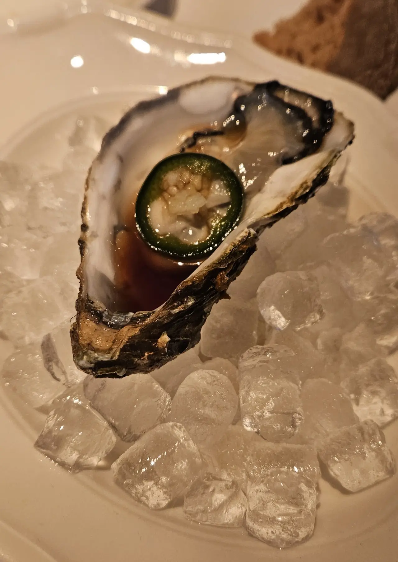 An oyster on ice topped with a small green garnish