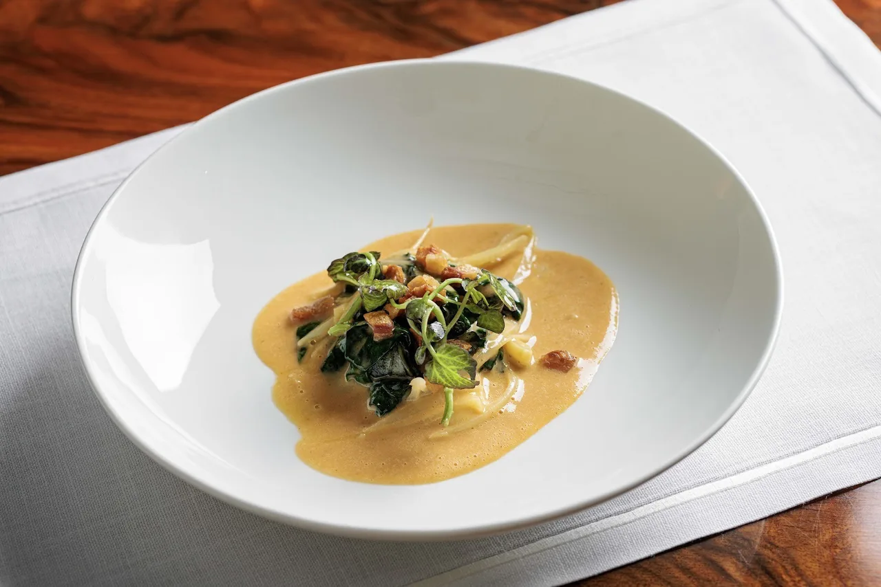 A white shallow bowl with a creamy sauce and greens
