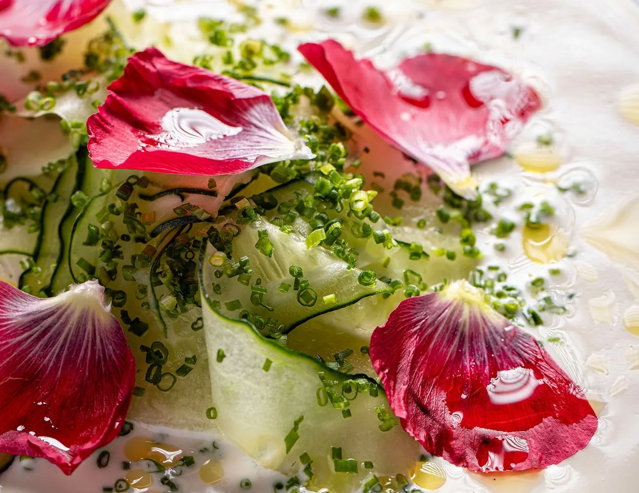 Slices of cucumber with red flower petals on a white plate