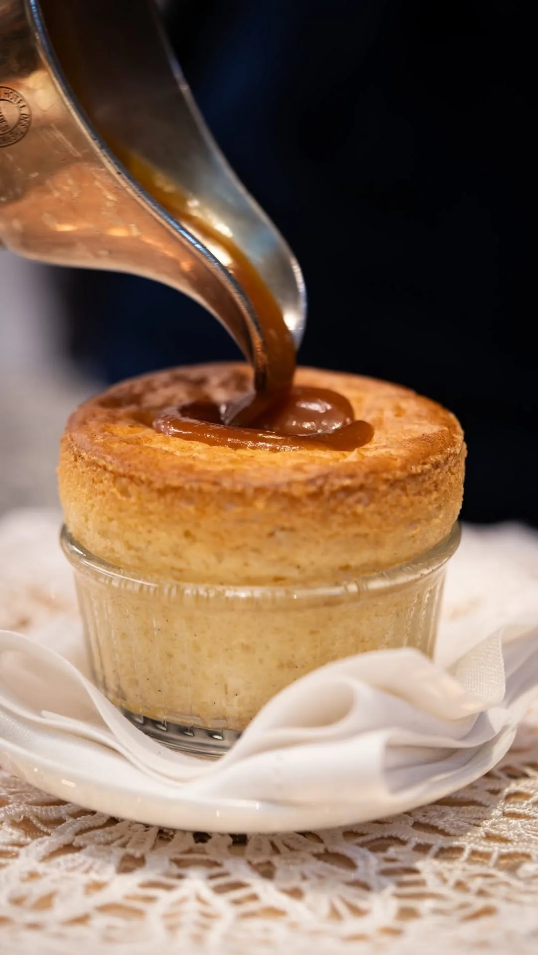 A small golden baked soufflé in a glass dish with dark sauce poured over it