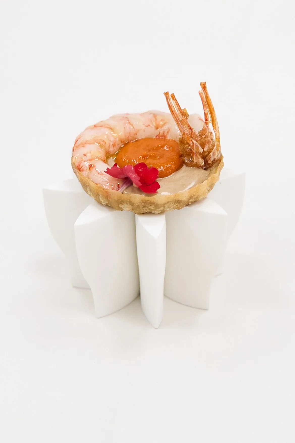 A prawn with an orange topping and a red flower on a white sculptural stand