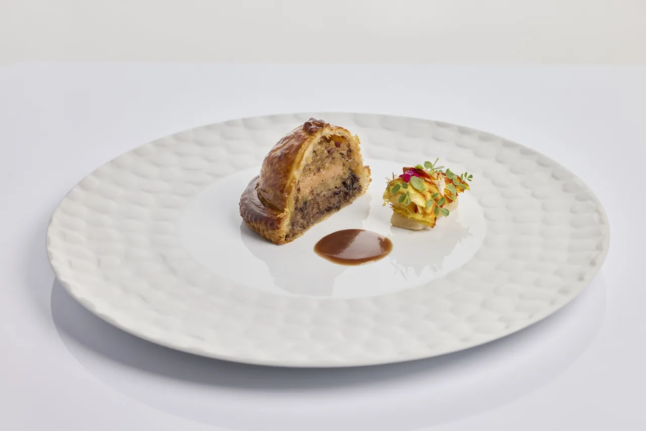 A round white plate with a pastry-wrapped portion and a small garnish beside it