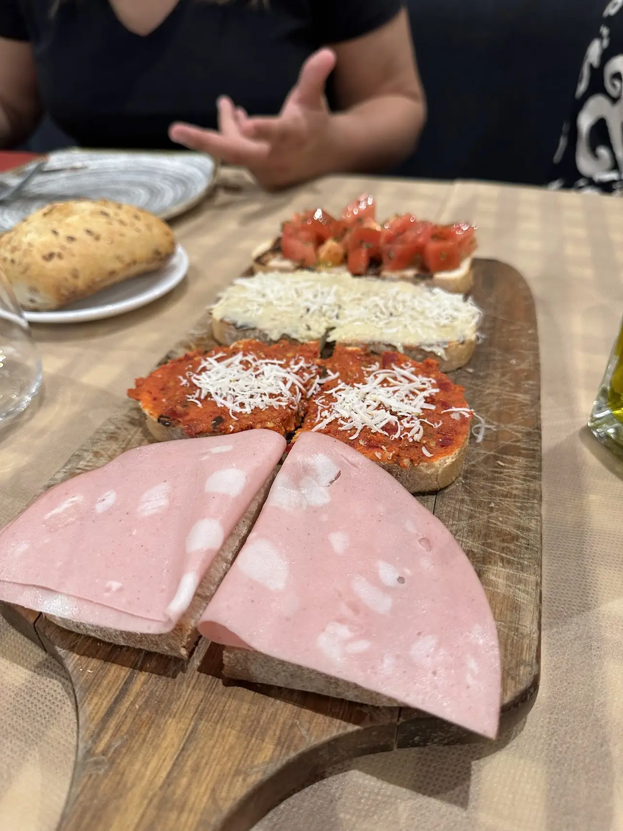 A wooden board with sliced mortadella and toasted bread topped with tomato and cheese